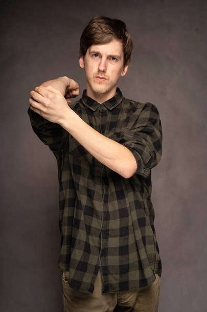 Young handsome tall slim white man with brown hair stretching with flannel shirt on grey background - Foto, Imagen