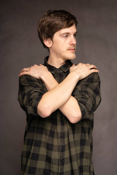 Young handsome tall slim white man with brown hair holding his shoulders with flannel shirt on grey background - Fotografie, Obrázek