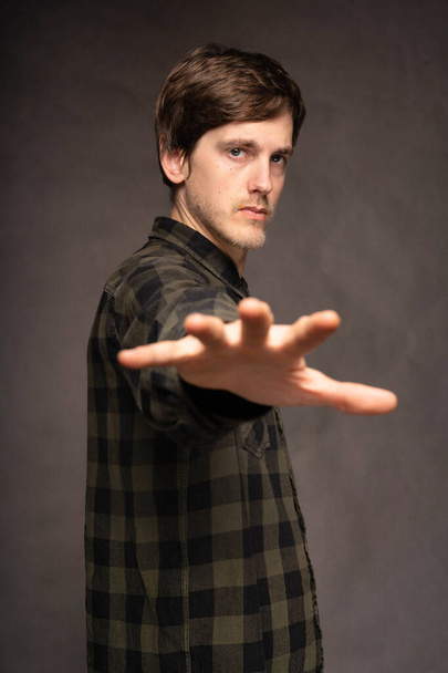 Young handsome tall slim white man with brown hair reaching out with his hand with flannel shirt on grey background - Foto, imagen