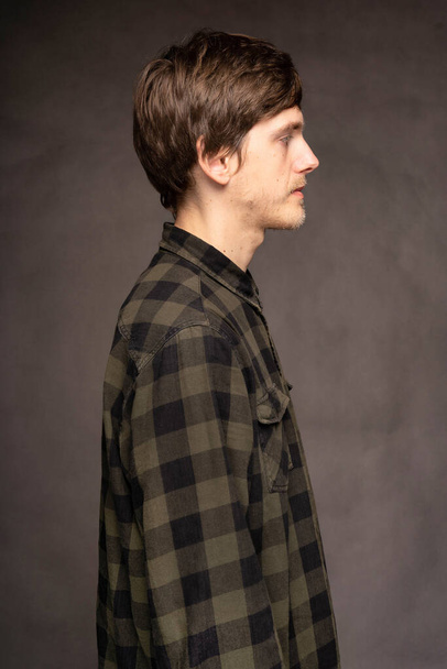 Young handsome tall slim white man with brown hair facing right with flannel shirt on grey background - Zdjęcie, obraz