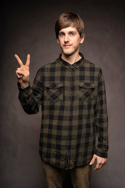Young handsome tall slim white man with brown hair making peace sign with hand with flannel shirt on grey background - Foto, Imagem