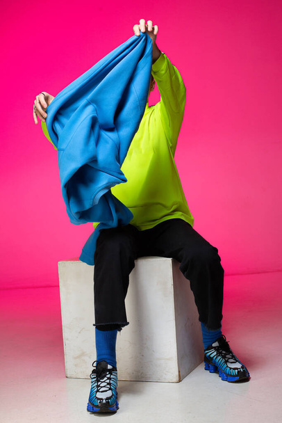 Young european boy with white skin isolated on pink taking off blue hoody - Φωτογραφία, εικόνα