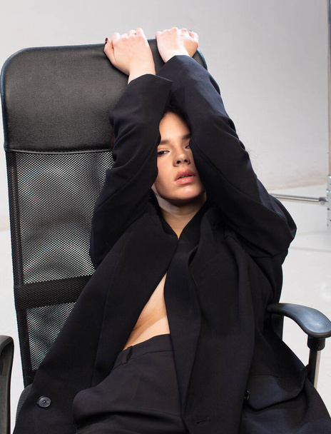Young european girl with white skin in office leather chair in black clothes - Фото, зображення