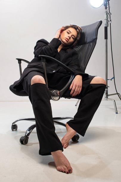 Dark long hair young european girl with white skin in office chair in black - Photo, Image