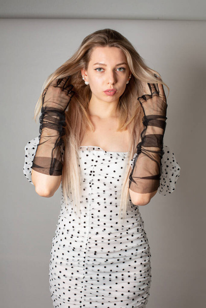 Young woman with blond hair and white skin isolated on dark grey in white dress with dots - Foto, Imagem