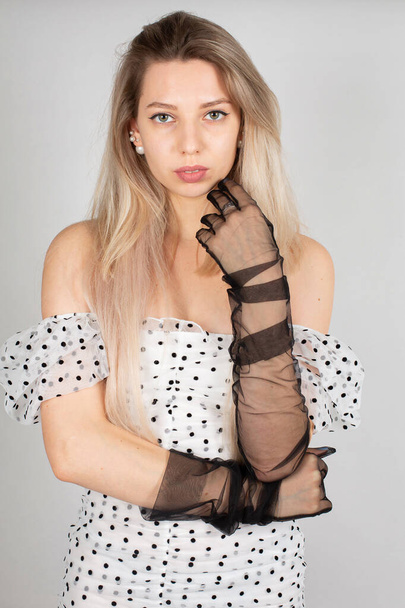 Young woman with blond hair and white skin isolated on grey in white dress in dots - Fotó, kép