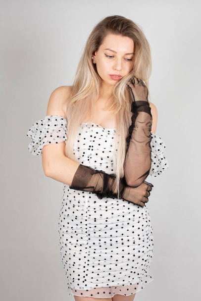 Young woman with blond hair and white skin isolated on grey in white polka dot dress - Foto, immagini