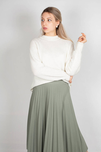 Woman with long hair and white skin isolated on grey in white sweater and olive skirt - 写真・画像