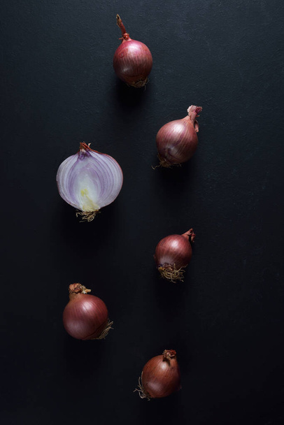 Small shallots onions and a halved on black background - Fotografie, Obrázek