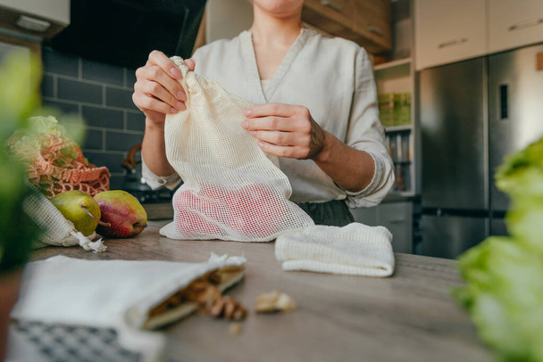 Mujer joven sosteniendo la bolsa de algodón orgánico reutilizable con pimientos en la mesa en la cocina. Cero residuos y concepto de embalaje sostenible. - Foto, imagen