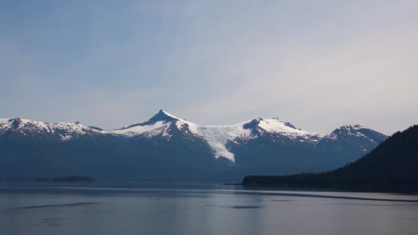 A hegy zöld fákkal. A háttérben egy hegy hóval. Alaszka fjordjai, egyedülálló természeti tájak. Alaszka, USA. 2019. június. - Felvétel, videó