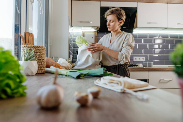 Jeune femme tenant un sac réutilisable en coton avec de la nourriture dans la cuisine. Concept zéro déchet et emballage durable. - Photo, image