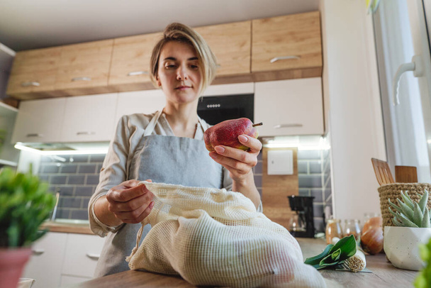 Fiatal nő kezében a bio pamut újrahasznosítható termék táska körte az asztalon a konyhában. Zéró hulladék és fenntartható csomagolás. - Fotó, kép