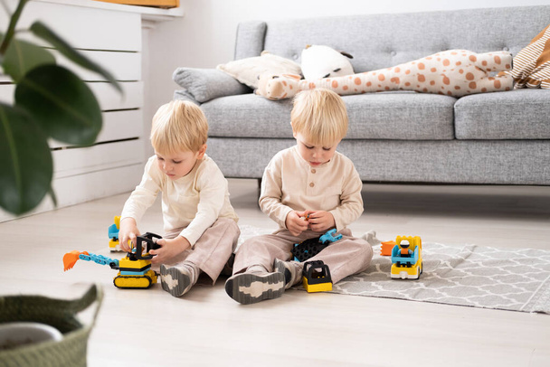 Dwóch zabawnych chłopców bracia bliźniacy bawiący się z konstruktorem samochodów zabawki w salonie - Zdjęcie, obraz