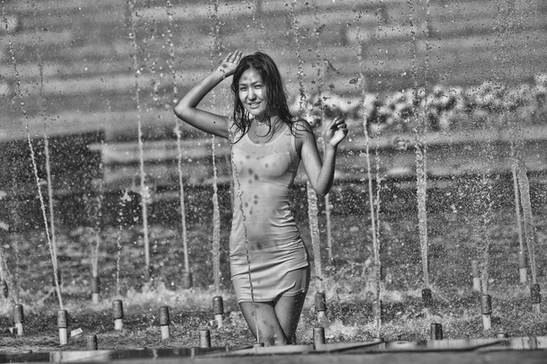 Chica en un vestido elegante con el pelo largo en gotitas de agua en la fuente de la ciudad
 - Foto, imagen