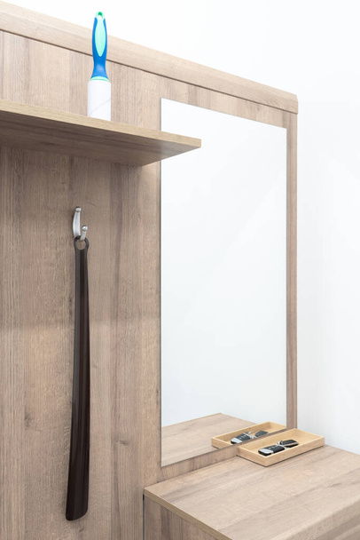 Wooden wall with a mirror, shoe horn hanging on a hanger and pet hair remover roller standing on a wooden board. Furniture next to entry door. Corridor equipment. - Foto, Bild