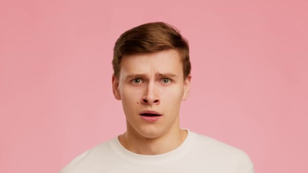 Anxious Young Man Expressing Fear Raising Eyebrows Over Pink Background - Кадры, видео