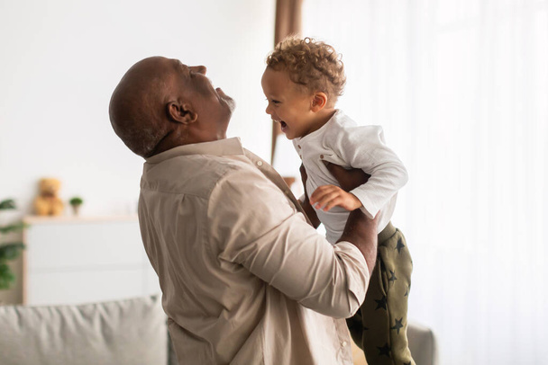 自宅で腕の中で小さな孫を持ち上げる楽しい黒の祖父 - 写真・画像