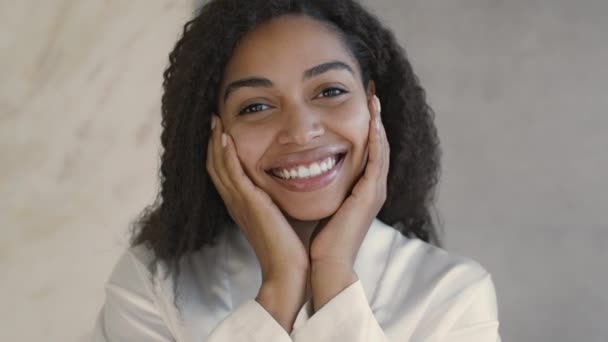 Natural beauty concept. Close up of young positive african american lady smiling at camera, touching her smooth cheeks - Video
