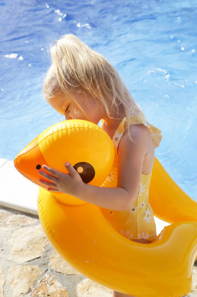 Little girl playing with yellow duck swimming inflatable pool seat float. Summertime lifestyle concept. - Photo, Image