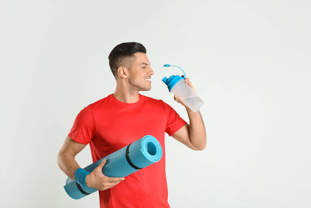 Handsome man with yoga mat drinking water on light background - Fotó, kép