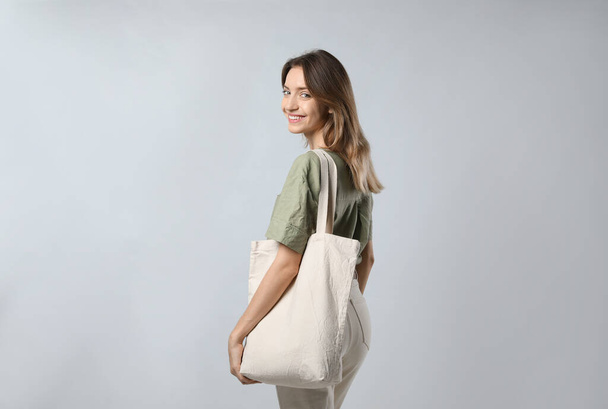 Happy young woman with blank eco friendly bag on light background - Fotografie, Obrázek