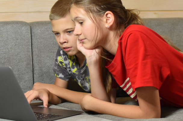 friendly children lie on the couch watching video in a laptop at home. distance learning online from home - Foto, immagini