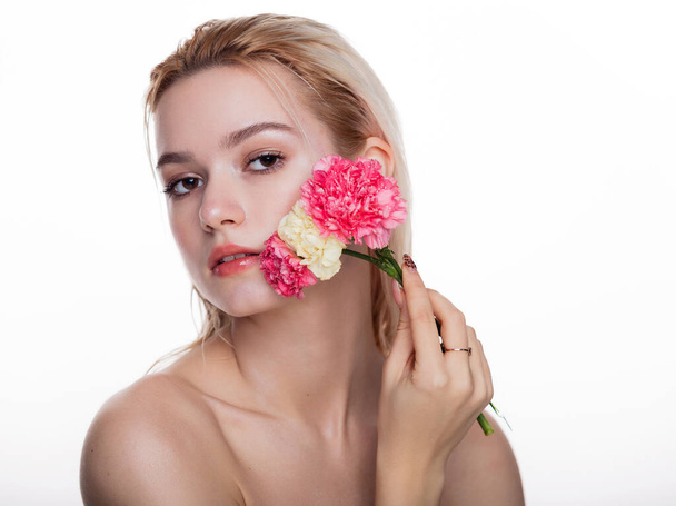 ピンクの花を持つ魅力的な若い女性。白の背景の上に隔離された顔に近いピンクの花を保持ブロンドモデル。美と医療の概念テキストのためのフリースペース - 写真・画像