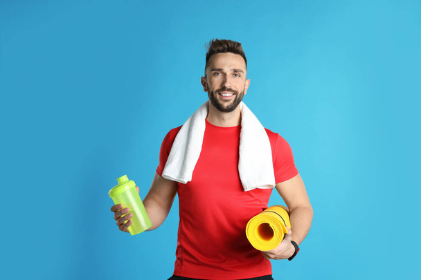 Beautiful man with yoga mat, towel and shaker on turquoise background - Photo, image