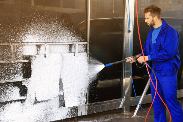 Worker cleaning auto mats with high pressure foam jet at car wash - Фото, изображение