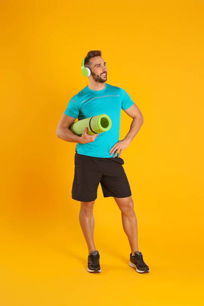 Handsome man with yoga mat and headphones on yellow background - Zdjęcie, obraz