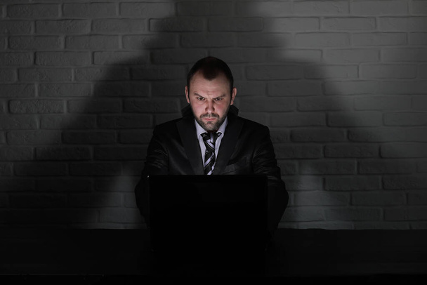 Hacker em máscara preta e capuz na mesa em frente ao monito - Foto, Imagem