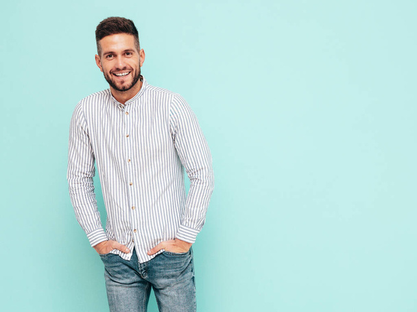 Portrait of handsome smiling model. Sexy stylish man dressed in shirt and jeans. Fashion hipster male posing near blue wall in studio - Φωτογραφία, εικόνα