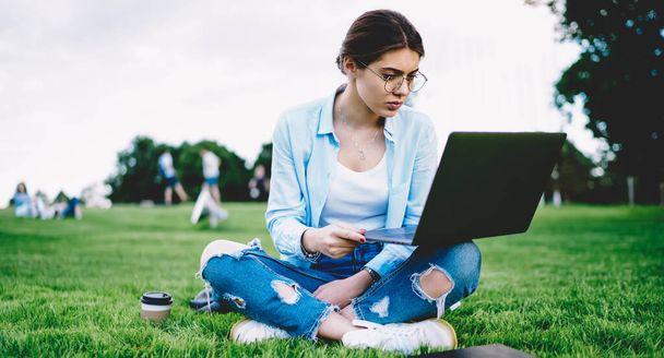 Skilled female student using wireless connection outdoors for watching educational webinar via laptop computer, Caucasian woman in classic eyewear networking social media during leisure in park - Foto, immagini