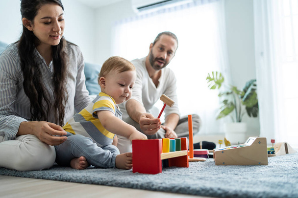 Kaukázusi boldog szülő játszani baba kisgyermek a nappaliban. Vonzó pár anya és apa nézi a fiatal csecsemő fiú gyermek fejlődését. Tevékenységi kapcsolat otthon a házban. - Fotó, kép
