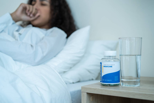 Young Latino sick woman in pajamas taking medicine before sleep on bed. Attractive young woman feeling unhappy and coughing in dark night in bedroom at home. Health care-medical lifestyles concept. - Foto, immagini