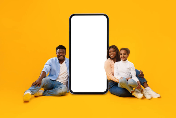 Black family showing white empty smartphone screen leaning on display - Photo, Image