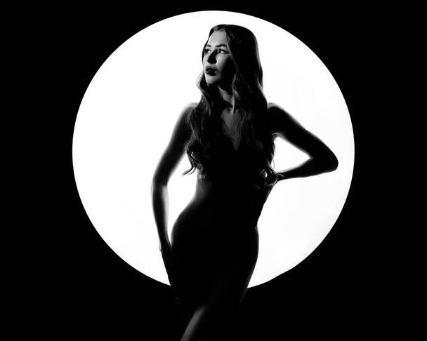 Black and white woman beauty line of body. Woman in white circle ring on black background. Perfect body, slim figure. Nude fashion woman posing in beam of searchlight. Art of erotica - Photo, Image