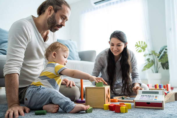 Caucasian loving parent looking at baby toddler playing in living room. Attractive couple mother and father watch young little infant son child's development. Activity relationship at home in house. - Foto, Imagem