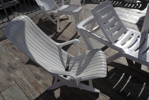 White plastic empty chairs and deck chairs stand on a wooden surface. - Photo, Image
