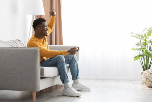 Joyful black guy sitting on couch with joystick - Photo, Image