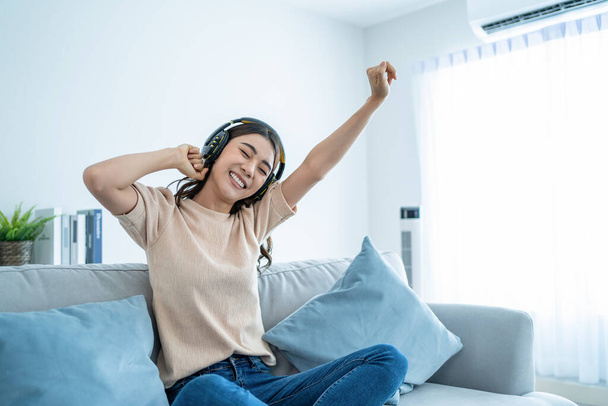 Asiatische lustige Frau hören Musik und tanzen auf dem Boden im Wohnzimmer. Attraktive schöne junge Mädchen setzen Kopfhörer auf und freuen sich, die Freizeit zu Hause zu verbringen und die Wochenendaktivität im Haus zu genießen - Foto, Bild