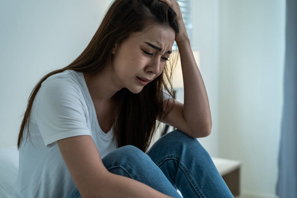 Asian beautiful depression girl crying in tears sit on bed in bedroom. Attractive unhappy young woman feeling sad lonely and upset with life problem and hold tissue on hands in dark night room at home - Fotó, kép