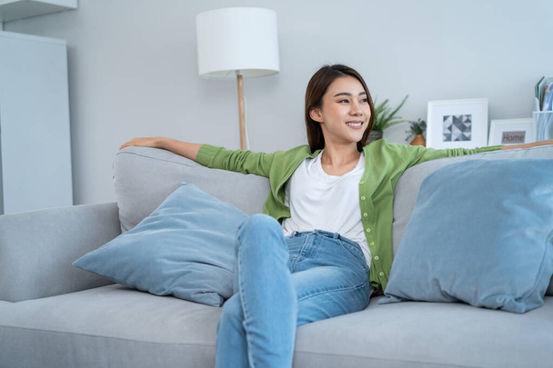 Asian beautiful woman jumping into comfort sofa in living room at home. Young attractive girl feeling happy and relax, enjoy health wellness holiday vacation to spend leisure free time alone in house. - Foto, Imagen