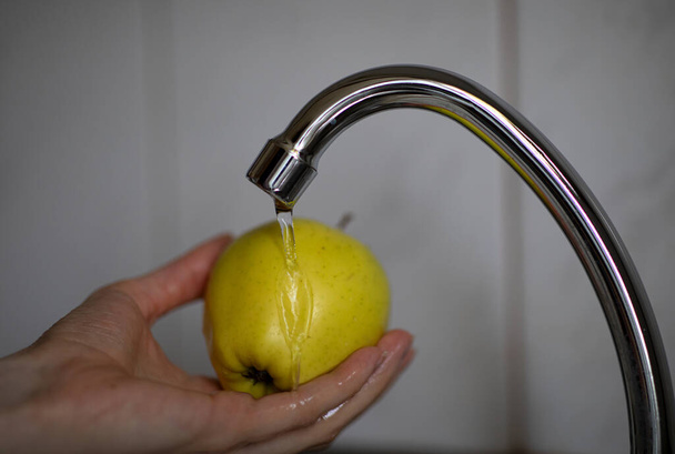 Washing the yellow apple under running tap water. A woman's hand washes an apple - Foto, immagini
