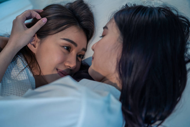 Asian beautiful lesbian couple lying down on bed and hugging each other. Attractive romantic girl friend in pajamas spending night leisure time together in bedroom. Homosexual freedom pride concept. - Valokuva, kuva