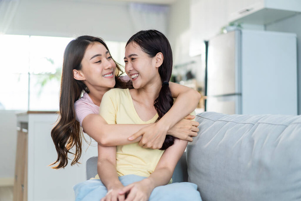 Asian beautiful lesbian women couple hugging girlfriend in living room. Attractive two female gay friend sitting on sofa in living room, feel happy and enjoy spending time together on holiday in house - Fotografie, Obrázek