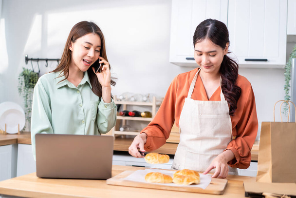 Asian beautiful business woman and friend bake bakery and sale in house. Attractive lesbian couple feel happy and exciting for success in entrepreneur sell food order from home then high five together - Photo, Image