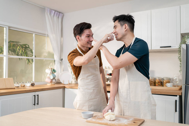 Asiático joven LGBTQ macho gay familia disfrutar de hornear panadería en cocina en casa. Atractivo guapo romántico hombre pareja usar delantal sentirse feliz y alegre a pasar el tiempo cocinando alimentos juntos en casa. - Foto, imagen