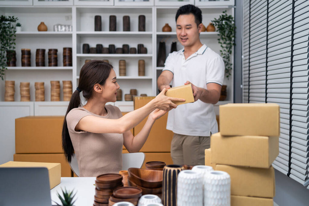 Asian man and woman packing vase goods order into box for customer. Young attractive business couple working to preparing parcel boxes checking ecommerce shipping online retail to sell at home store. - Foto, afbeelding